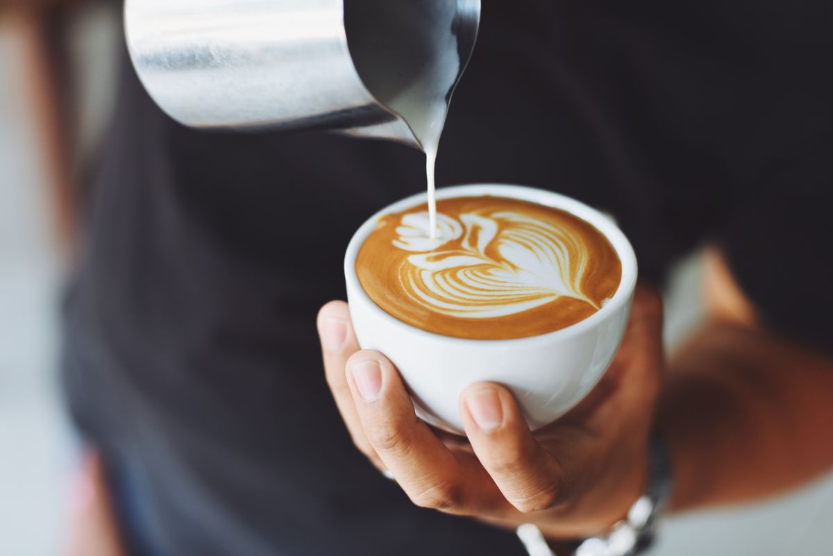 A barista pouring milk into a cup to make latte art
